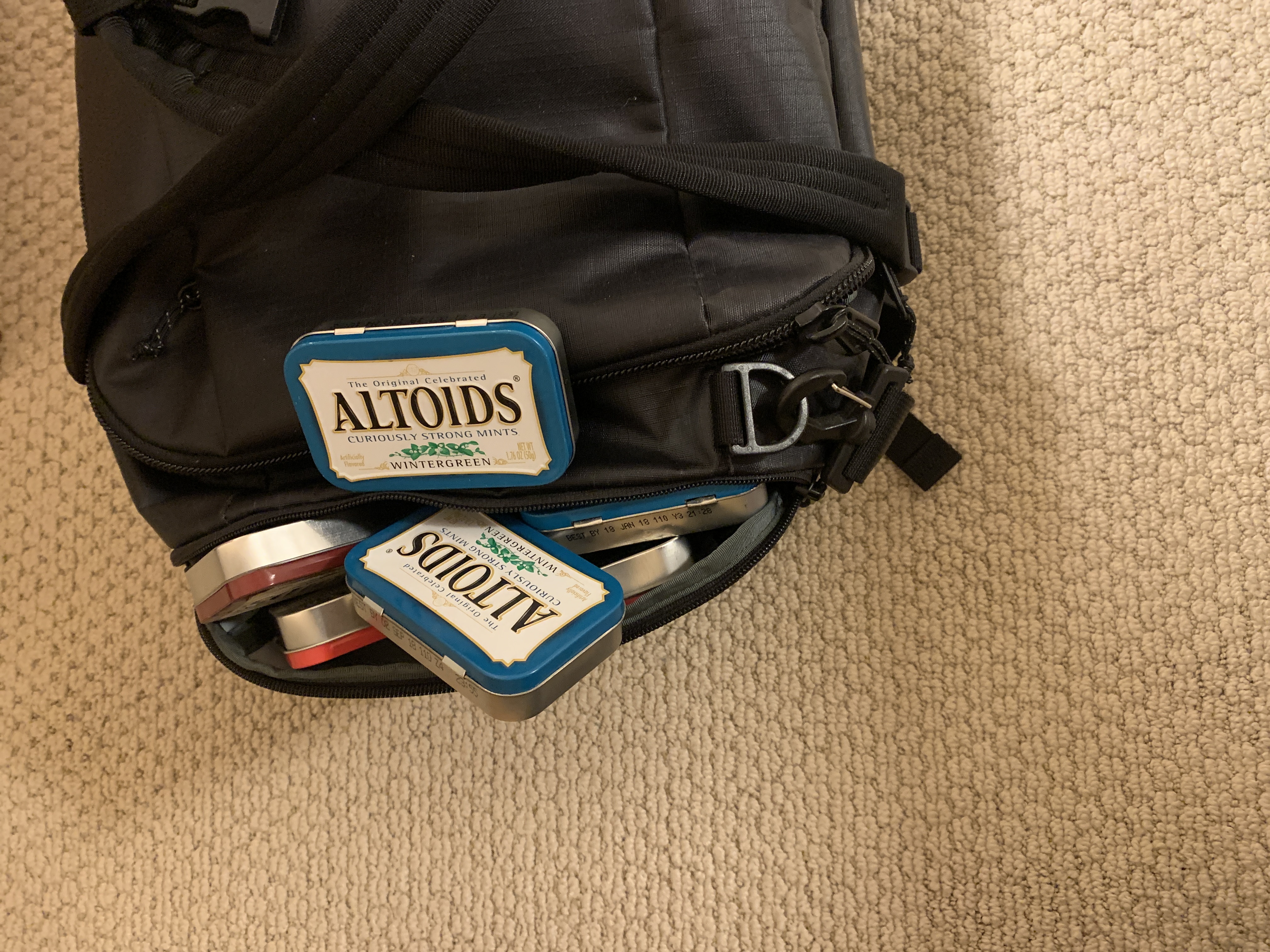 A picture of Altoids tins spilling out of the side pocket of a duffel bag.